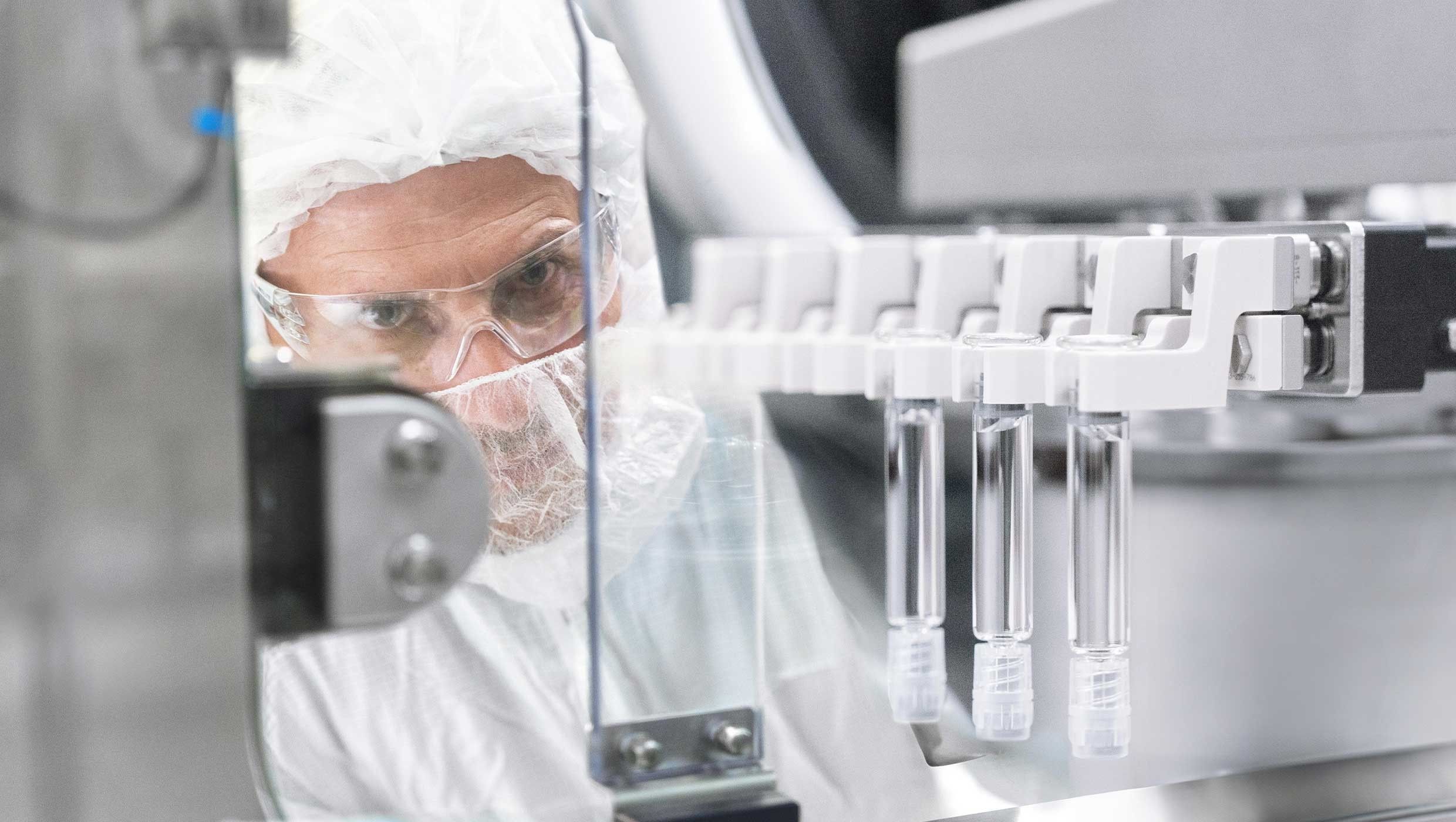 An employee wearing a hairnet and safety glasses observes as PFS machine in a pharmaceutical sterile and aseptic fill-finish manufacturing facility.
